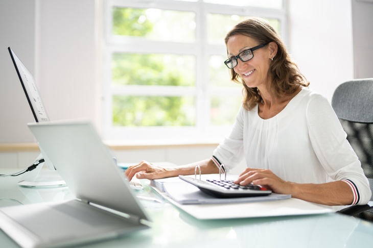 Person mit Brille sitzt an einem Schreibtisch und arbeitet mit einem Laptop