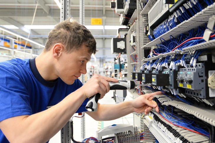 Person mit Schraubmaschine repariert Board mit elektrotechnischen Apparaturen