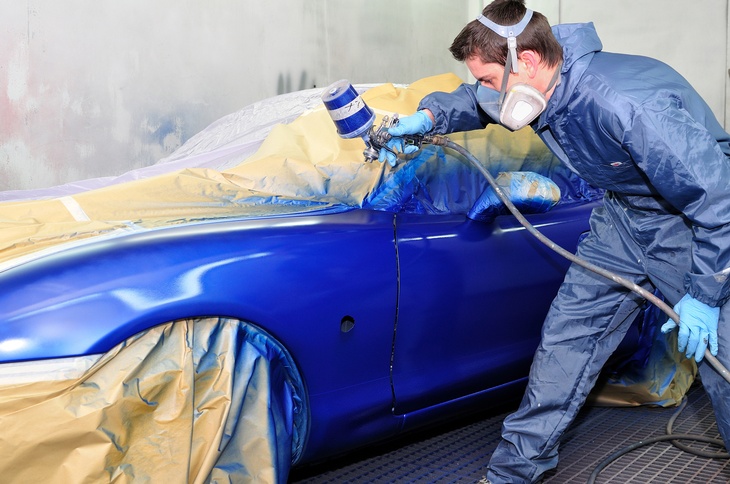 Person mit blauer Schutzkleidung lackiert ein blaues Auto