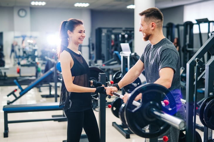 Zwei lachende Personen stehen in Fitnessstudio an Gewichtstemmgerät